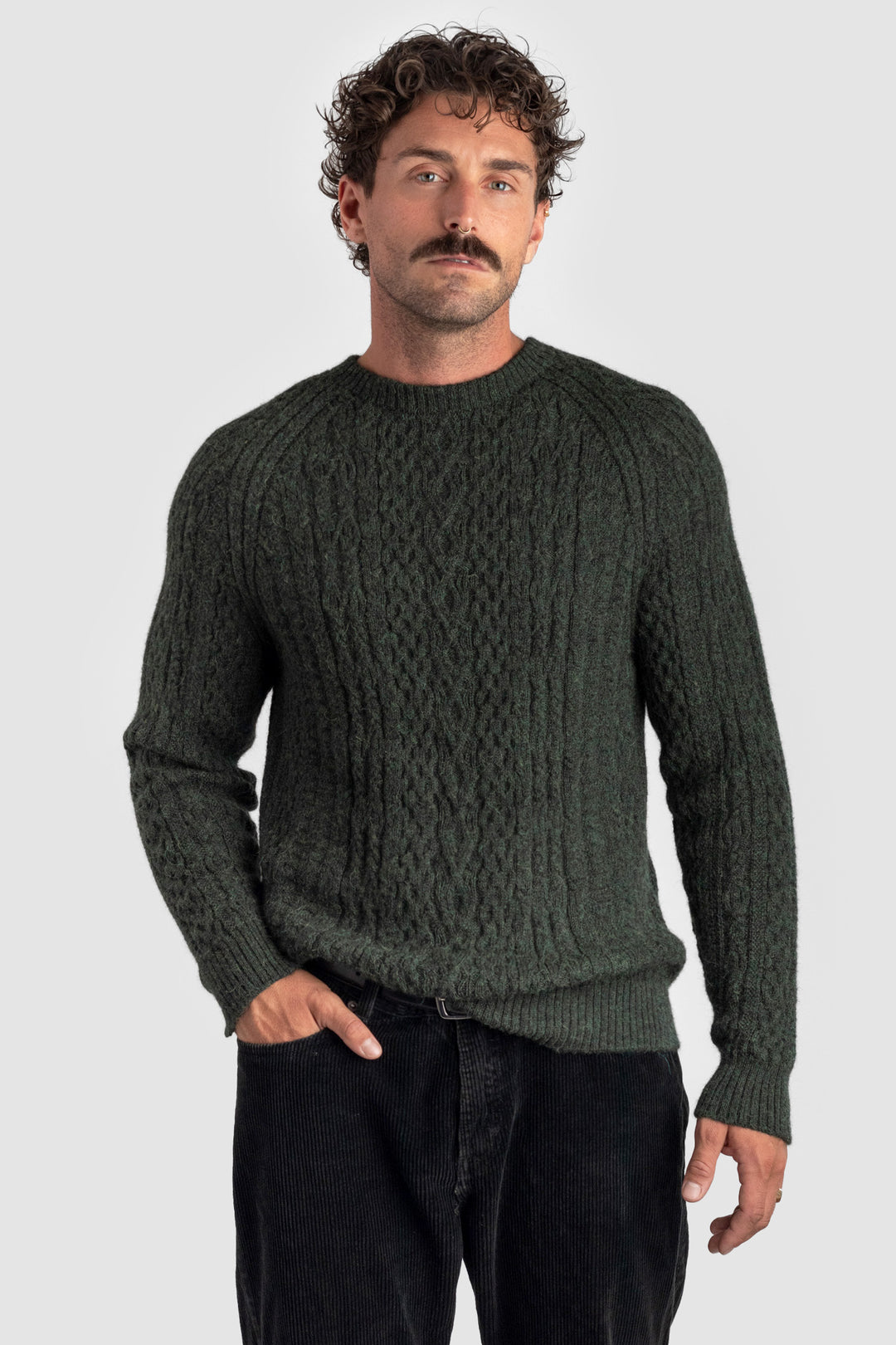 Man wearing a dark green cable knit sweater against a light gray background #colour_pine