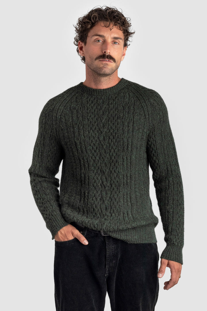 Man wearing a dark green cable knit sweater against a light gray background #colour_pine
