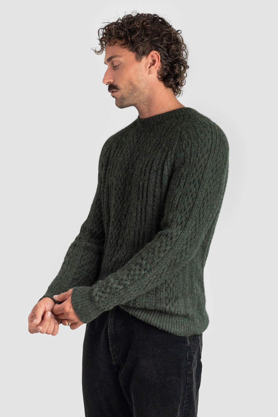 Man wearing a green cable knit sweater against a light gray background #colour_pine