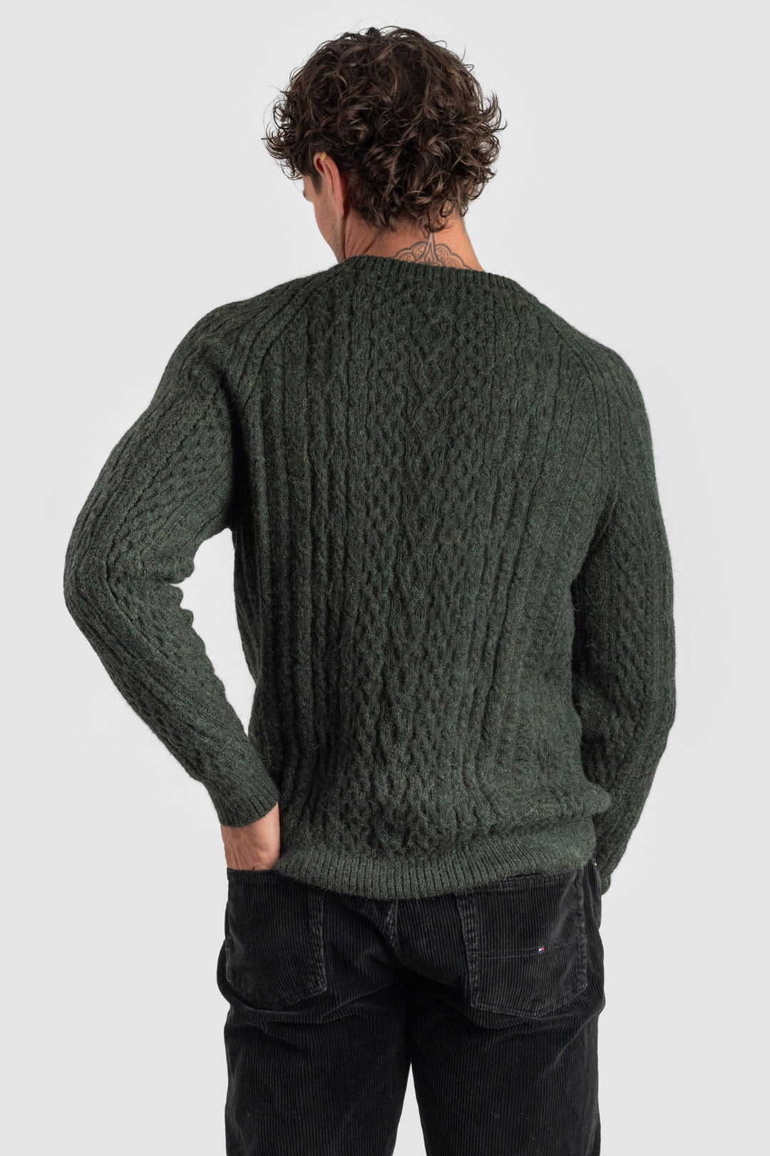 Person wearing a green cable knit sweater on a white background #colour_pine