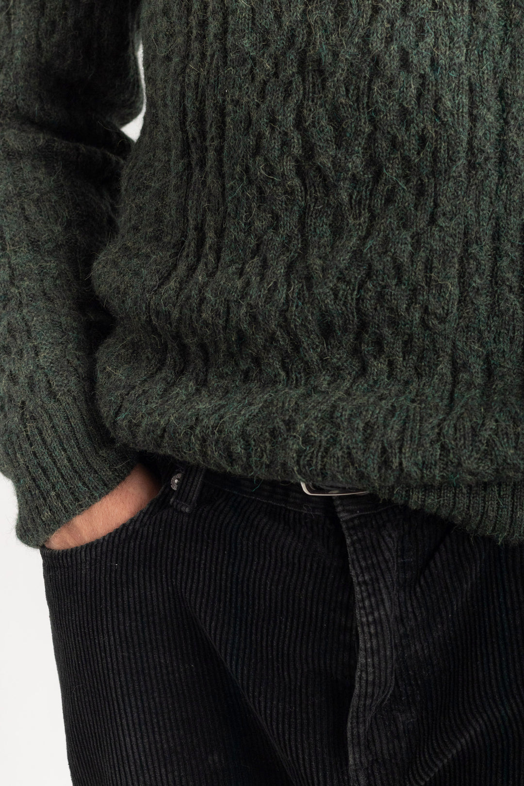 Person wearing a dark green cable knit sweater and black pants on a light background #colour_pine