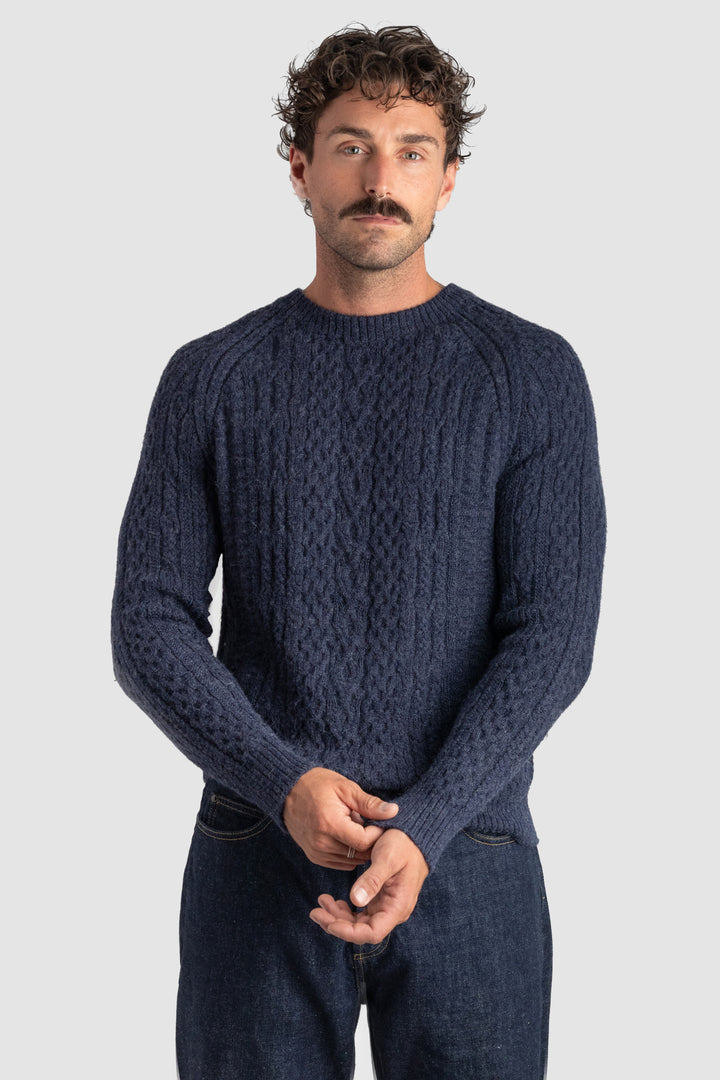 Man wearing a dark blue cable knit sweater on a light gray background #colour_navy