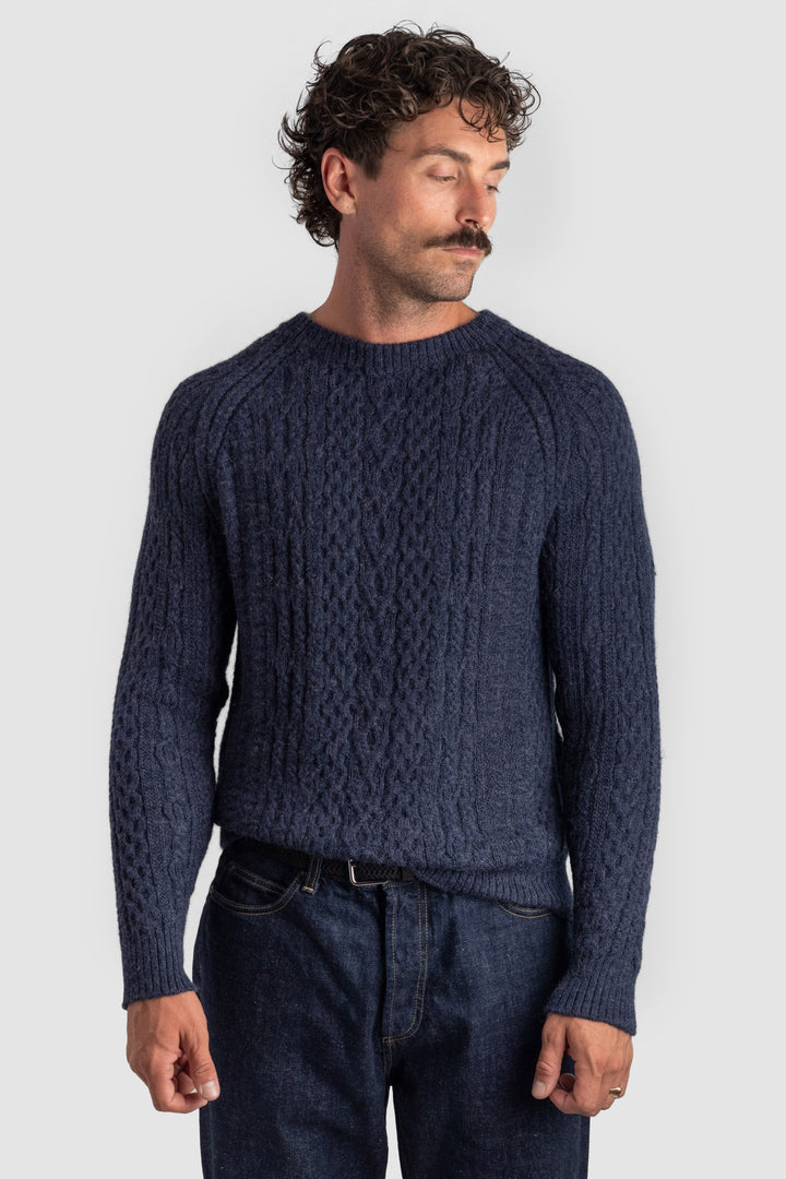 Man wearing a navy blue cable knit sweater against a light gray background #colour_navy