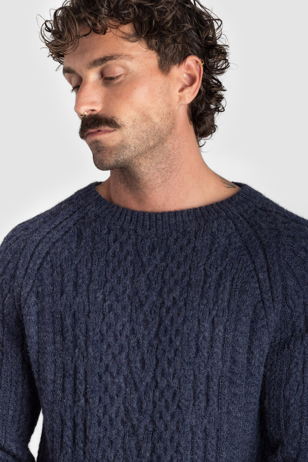 Man wearing a dark blue knitted sweater against a plain background #colour_navy