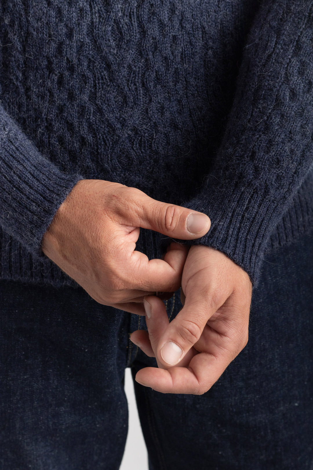 Close-up of hands wearing a dark blue knitted sweater against a neutral  background #colour_navy