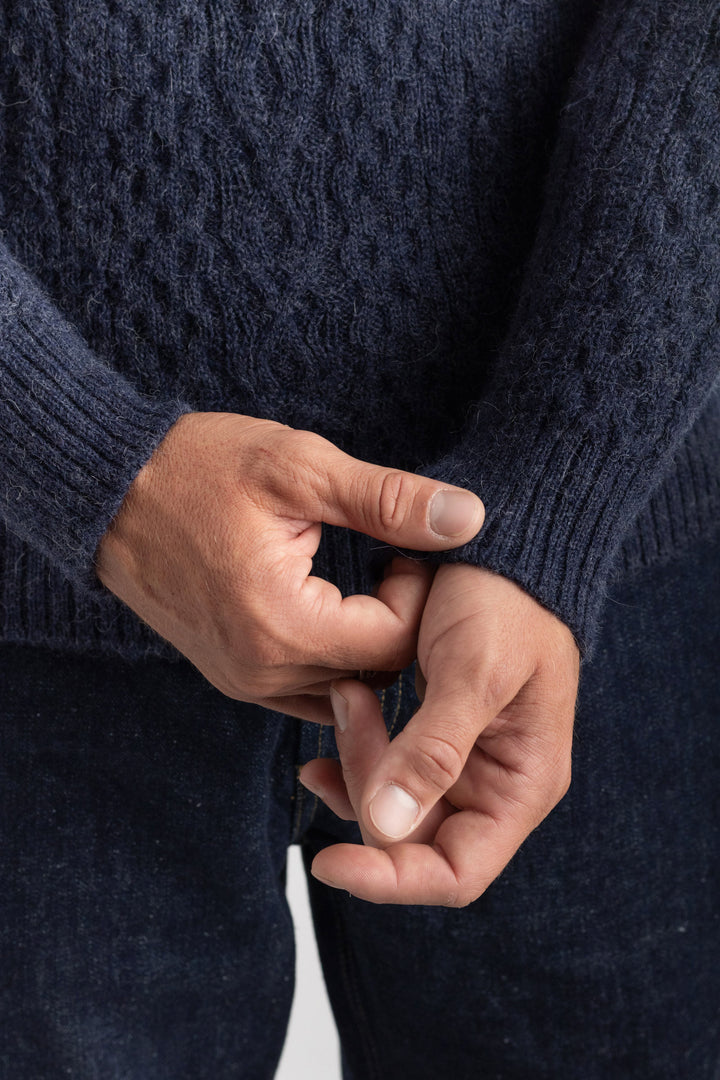 Close-up of hands wearing a dark blue knitted sweater against a neutral  background #colour_navy