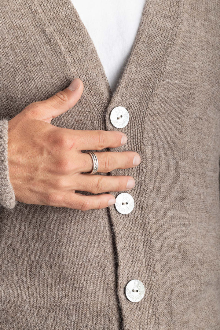 Close-up of a person wearing a gray cardigan with white buttons, touching one of the buttons. #colour_fawn