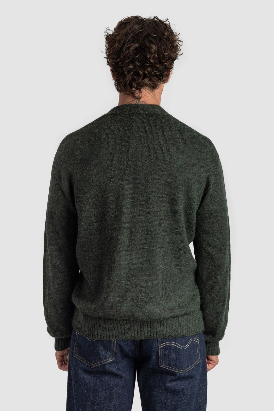 Person wearing a dark green sweater and jeans on a white background #colour_pine