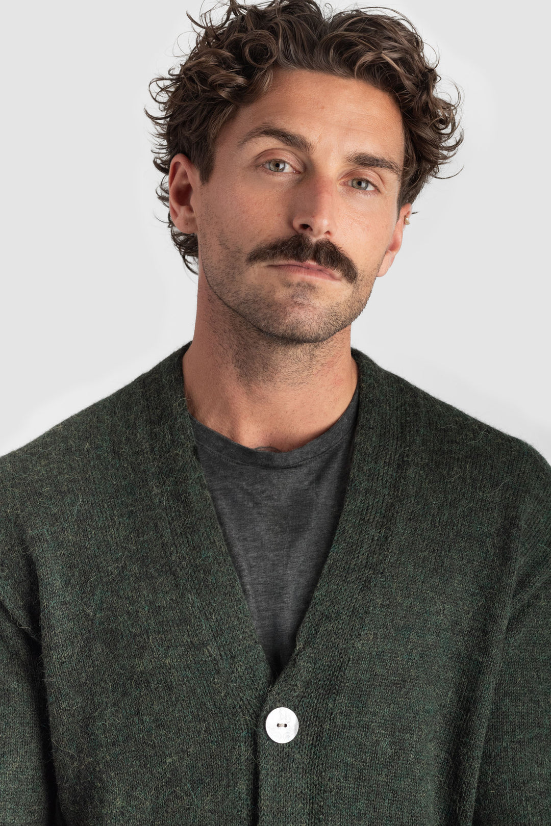 Man wearing a dark green cardigan over a gray shirt against a light gray background #colour_pine