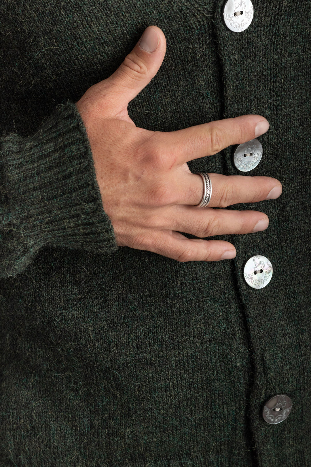 Hand resting on a dark green cardigan with buttons #colour_pine