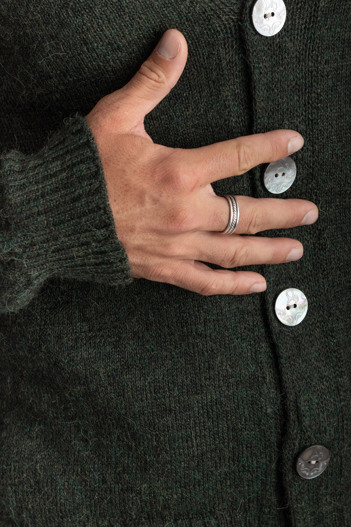 Hand resting on a dark green cardigan with buttons #colour_pine