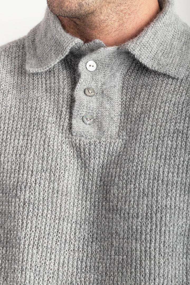Close-up of a person wearing a gray knitted sweater over a buttoned shirt. #colour_cool-grey