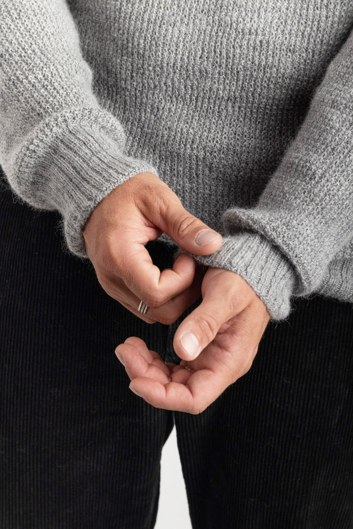Person wearing a gray sweater adjusting the sleeve on a white background #colour_cool-grey