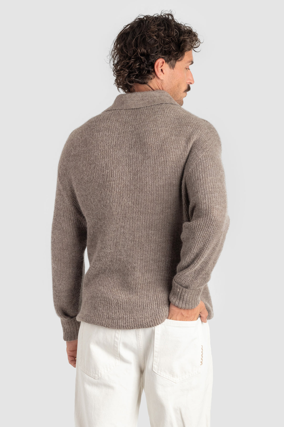 Man wearing a brown ribbed sweater and white pants on a light gray background #colour_fawn